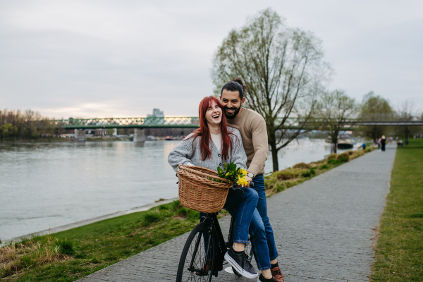 Boyfriend giving ride to his girlfriend on bicycle, sitting on frame. Beautiful couple on romantic date during cold spring or autumn day.