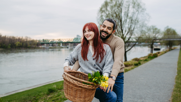 Boyfriend giving ride to his girlfriend on bicycle, sitting on frame. Beautiful couple on romantic date during cold spring or autumn day.