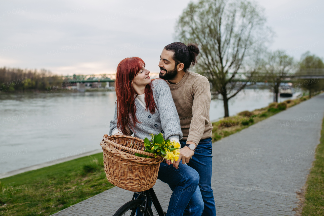 Boyfriend giving ride to his girlfriend on bicycle, sitting on frame. Beautiful couple on romantic date during cold spring or autumn day.