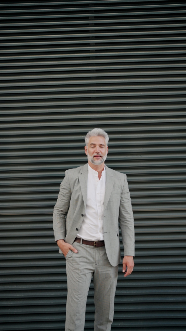 Portrait of mature businessman in grey suit with black blinds in background, looking into camera.