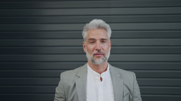 Mature businessman in grey suit with black blinds in background, looking into camera.