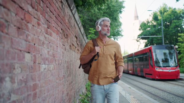 Commuter walking on street with phone and headphones. Tram passing by.