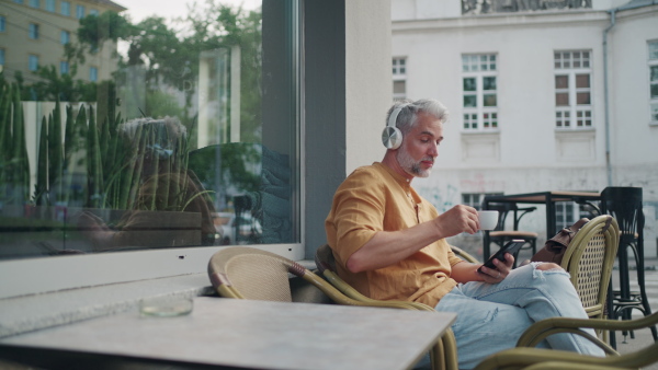 Man enjoying coffee in city, using smartphone and listening music.