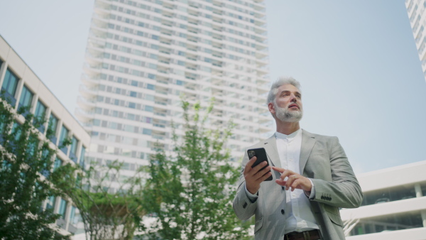 Portrait of mature businessman using smart phone outside office buildings . Low Angle view.