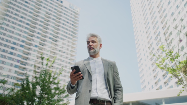 Portrait of mature businessman using smart phone outside office buildings . Low Angle view.