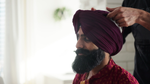 A close up of Indian man tying turban on man head. Video of handsome Indian man with turban.