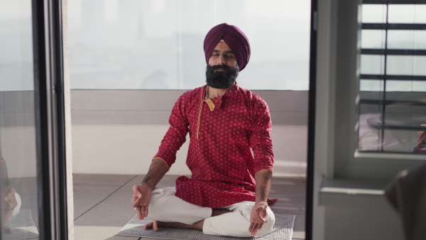 A man sitting on terrace, praying, meditating at home in the morning. Video of handsome Indian man with turban.