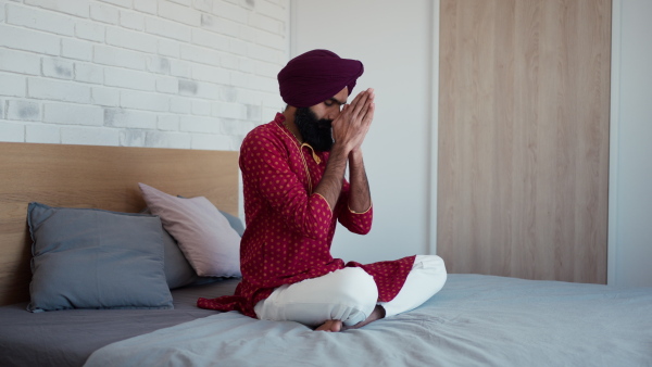 A man sitting in bedroom praying, meditating at home in the morning. Video of handsome Indian man with turban.