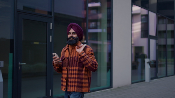 An young Indian man holding smartphone on city street. Video of handsome Indian man with turban, text messaging.