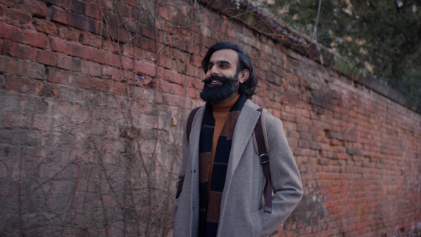 An young Indian man walking through the city during cold spring day. Video of handsome indian man in coat, phone calling smiling.