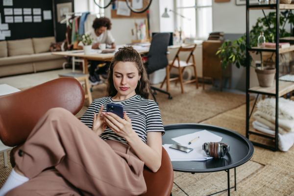 Young woman having break at work, scrolling her smartphone.