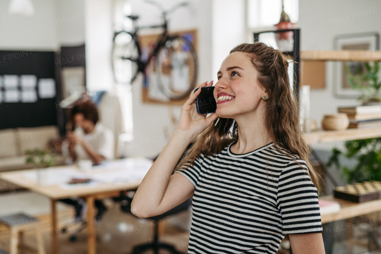 Young smiling woman calling in office, his colleague sitting in the background.