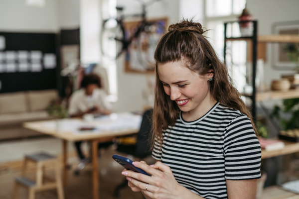 Young woman having break at work, scrolling her smartphone.