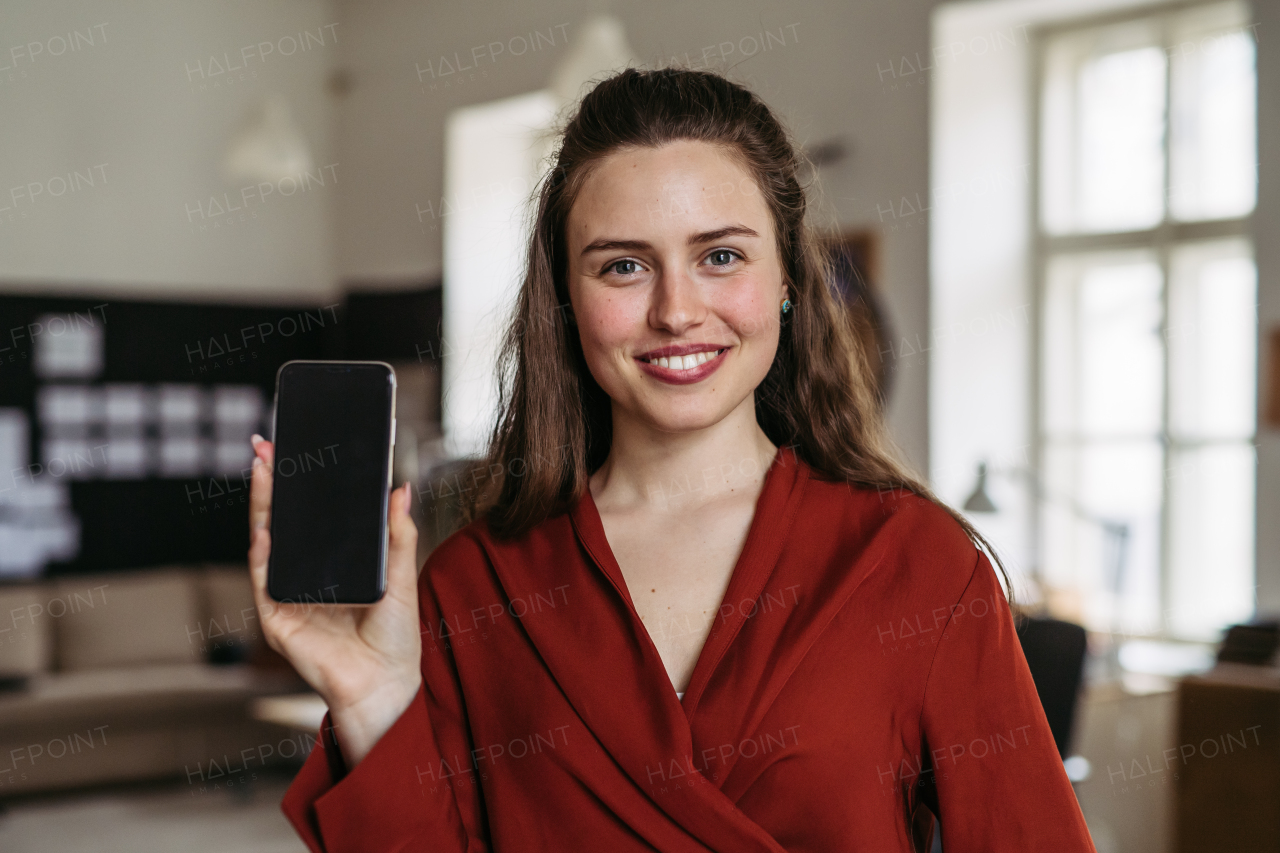 Portrait of young smiling woman with smartphone in office.