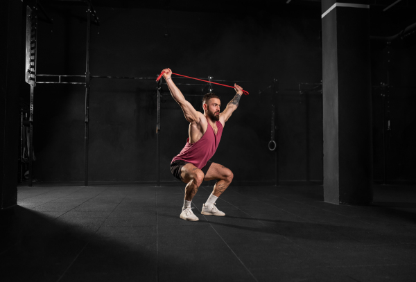 Strong man performing overhead squat, pressing barbell up, standing up from squating. Routine workout for physical and mental health.