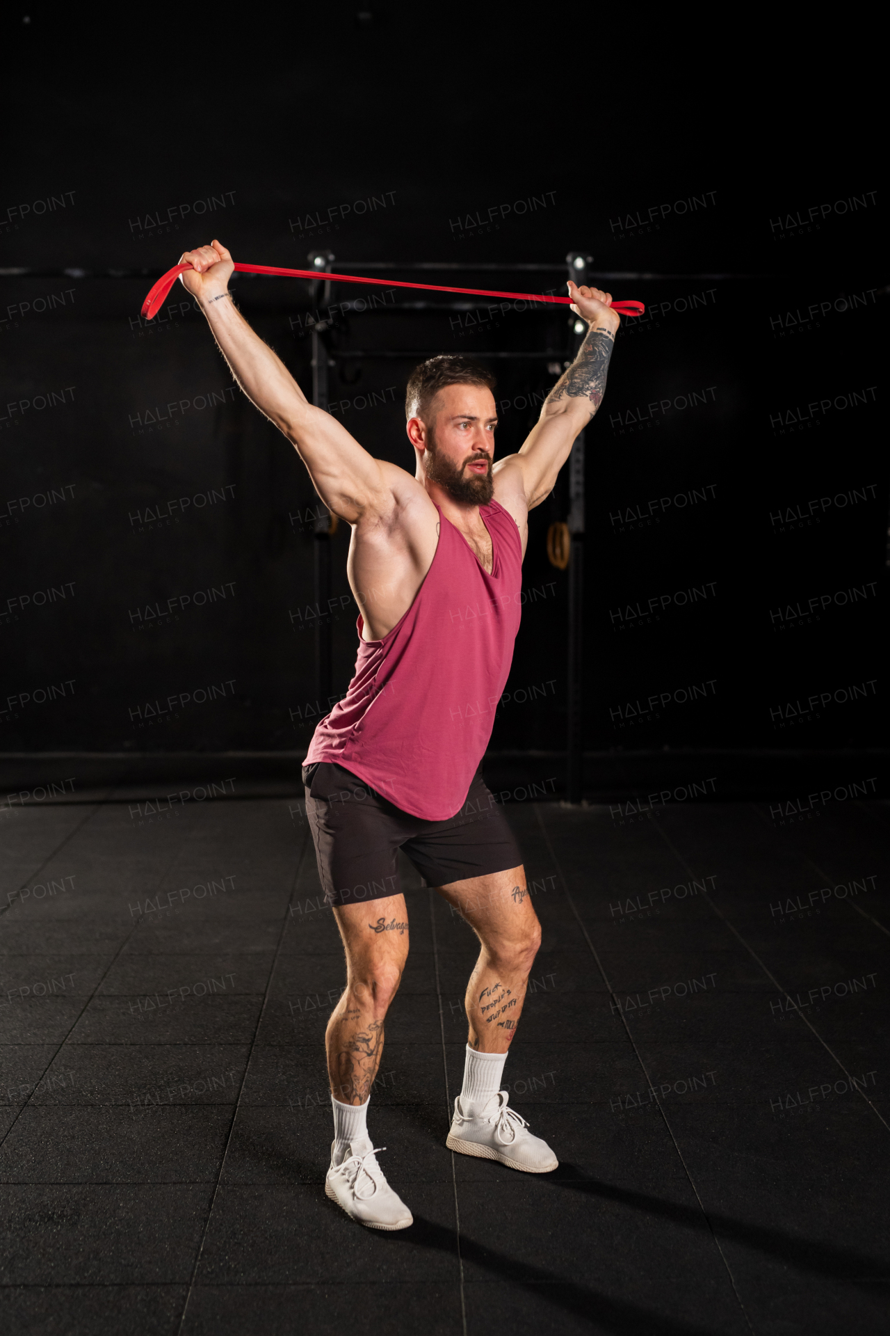 Portrait of handsome muscular man training with resistance band in gym, squatting. Routine workout for physical and mental health.