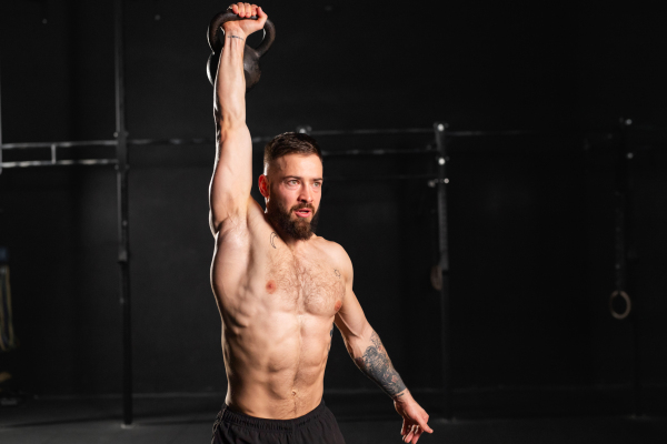 Man lifting a weight with hand, one arm dumbbell snatch, wearing only shorts, bare chest. Routine workout for physical and mental health.