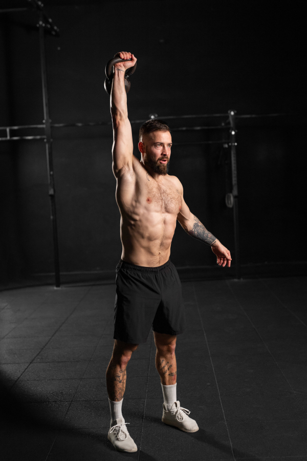 Man lifting a weight with hand, one arm dumbbell snatch, wearing only shorts, bare chest. Routine workout for physical and mental health.