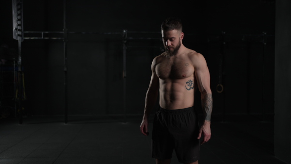 Man lifting dumbbell from gym floor, wearing only shorts, bare chest. Routine workout for physical and mental health.