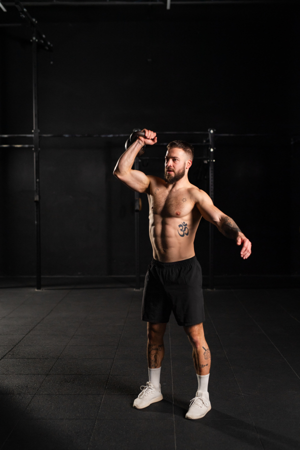 Man lifting a weight with hand, one arm dumbbell snatch, wearing only shorts, bare chest. Routine workout for physical and mental health.