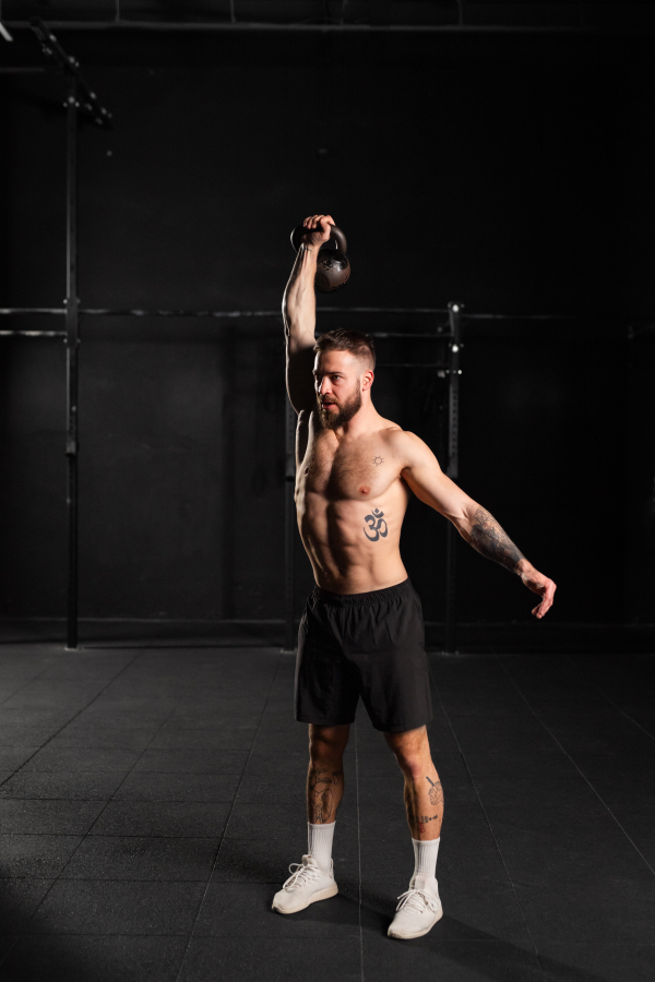 Man lifting a weight with hand, one arm dumbbell snatch, wearing only shorts, bare chest. Routine workout for physical and mental health.