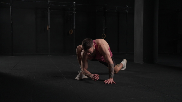 Video of handsome muscular man stretching his body, squatting, in gym. Routine workout for physical and mental health.