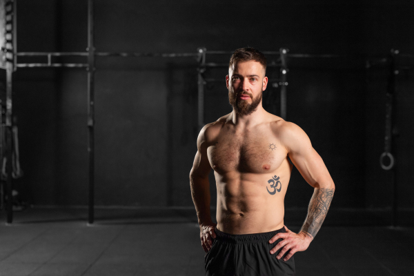 Portrait of handsome muscular man in gym with bare chest. Routine workout for physical and mental health.