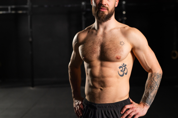 Portrait of handsome muscular man in gym with bare chest. Routine workout for physical and mental health.