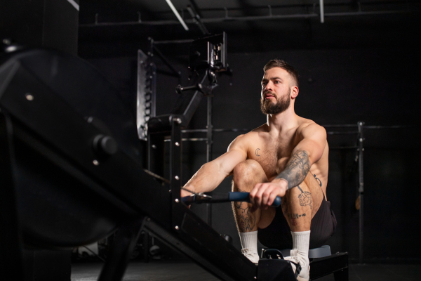 Man exercising on rowing machine, wearing only shorts, bare chest. Routine workout for a physical and mental health.