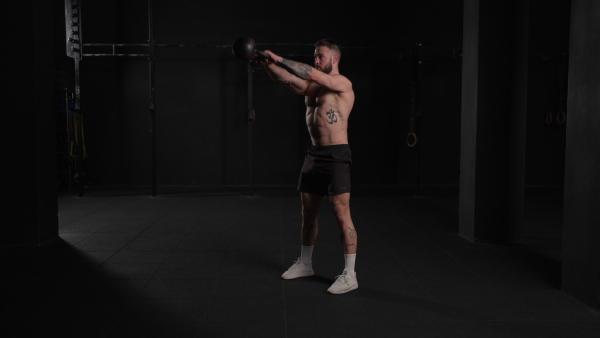 Man lifting dumbbell from gym floor, wearing only shorts, bare chest. Routine workout for physical and mental health.