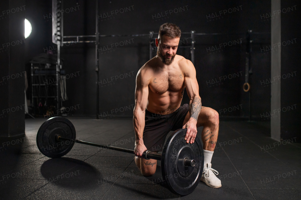 Strong man preparing for barbell lift, changing plates, loading the barbell. Routine workout for physical and mental health.