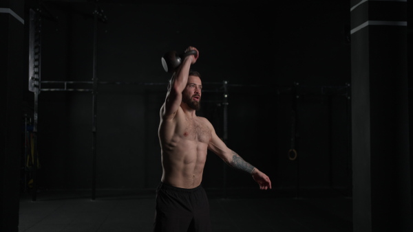 Man lifting a weight with hand, one arm dumbbell snatch, wearing only shorts, bare chest. Routine workout for physical and mental health.