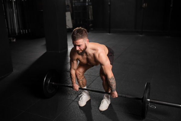 Strong man performing deadlift, lifting barbell from ground, full length shot. Strength exercise. Routine workout for physical and mental health.