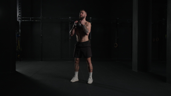 Man lifting dumbbell from gym floor, wearing only shorts, bare chest. Routine workout for physical and mental health.