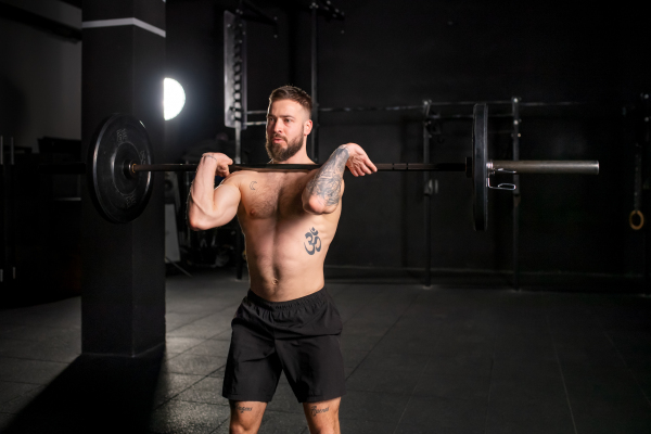 Strong man performing front squat, barbell resting on front shoulders, bare chest. Routine workout for physical and mental health.