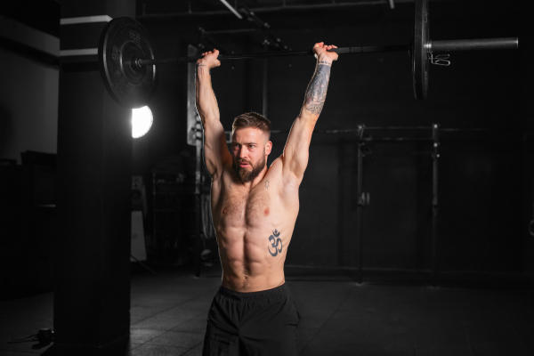 Strong man performing overhead squat, pressing barbell up, front waist up shot. Routine workout for physical and mental health.