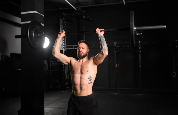 Strong man performing overhead squat, pressing barbell up, front body length shot. Routine workout for physical and mental health.