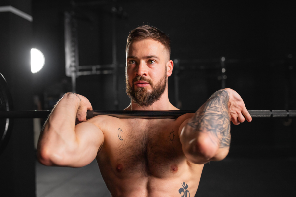 Strong man performing front squat, barbell resting on front shoulders, bare chest. Routine workout for physical and mental health.