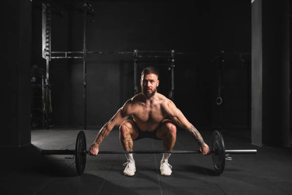 Strong man performing deadlift, lifting barbell from ground, full length shot. Strength exercise. Routine workout for physical and mental health.