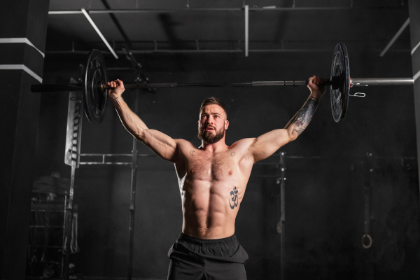 Strong man performing overhead squat, pressing barbell up, front waist up shot. Routine workout for physical and mental health.