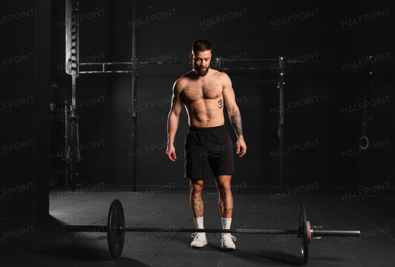 Strong man preparing for a barbell lift, overhead squat, standing by barbell. Routine workout for physical and mental health.