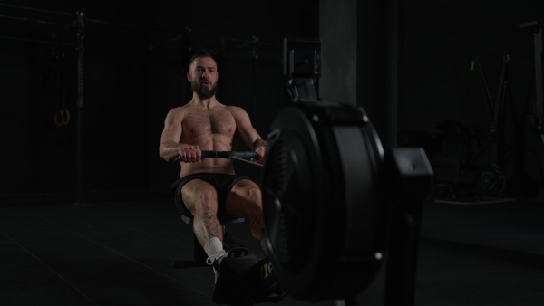 Man exercising on rowing machine, wearing only shorts, bare chest. Routine workout for a physical and mental health.