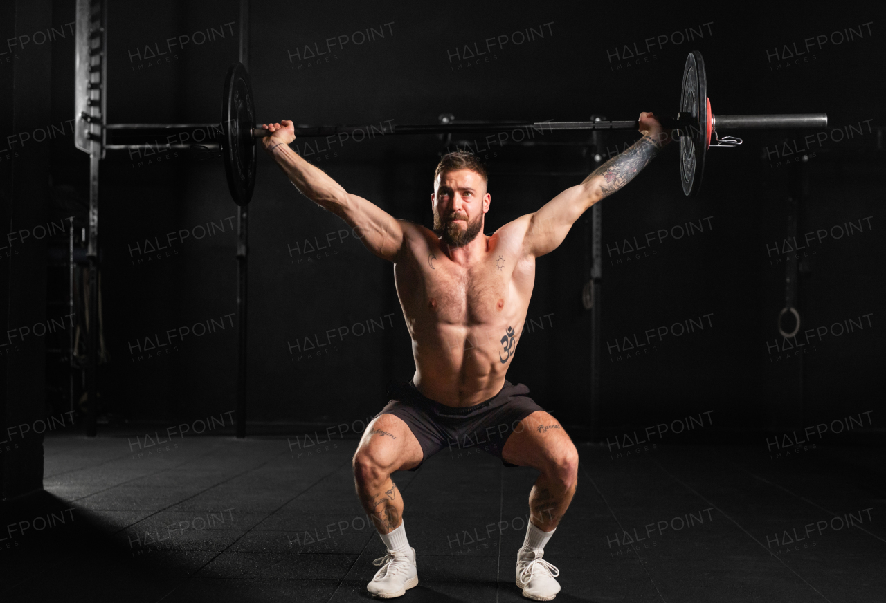 Strong man performing overhead squat, pressing barbell up, front body length shot. Routine workout for physical and mental health.