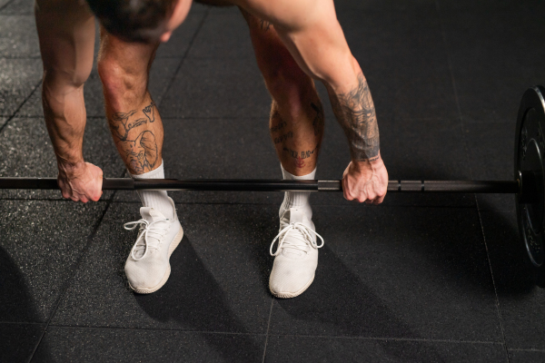 Strong man performing deadlift, lifting barbell from ground, full length shot. Strength exercise. Routine workout for physical and mental health.