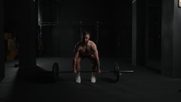 Strong man performing deadlift, lifting barbell from ground, full length shot. Strength exercise. Routine workout for physical and mental health.