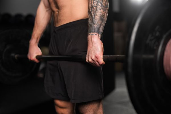 Strong man holding barbell in front his navel, close up. Routine workout for physical and mental health.