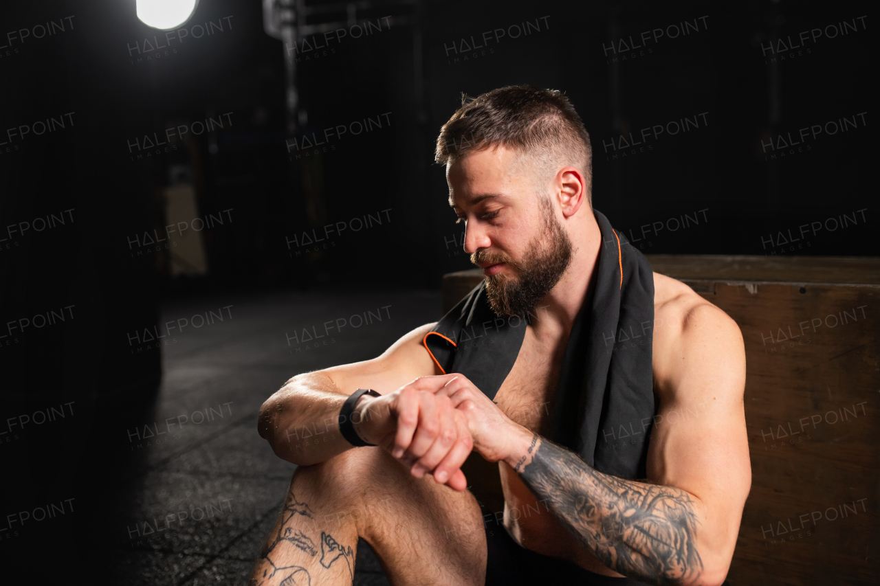 Handsome muscular man checking his performance on smartwatch, resting after a training in gym. Routine workout for physical and mental health.