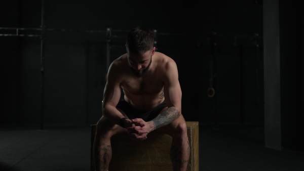 Muscular man resting after exercise, sitting, wearing short with bare chest. Routine workout for physical and mental health.