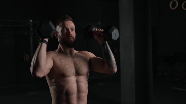 Man lifting dumbbellr, wearing only shorts, bare chest. Routine workout for physical and mental health.