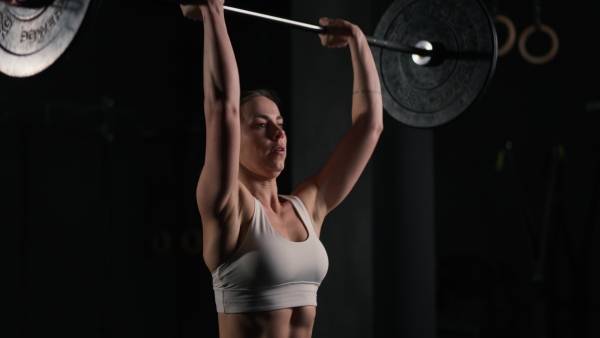 Front view of young muscular woman holding, pressing barbell up. wearing sportswear. Routine workout for physical and mental health.